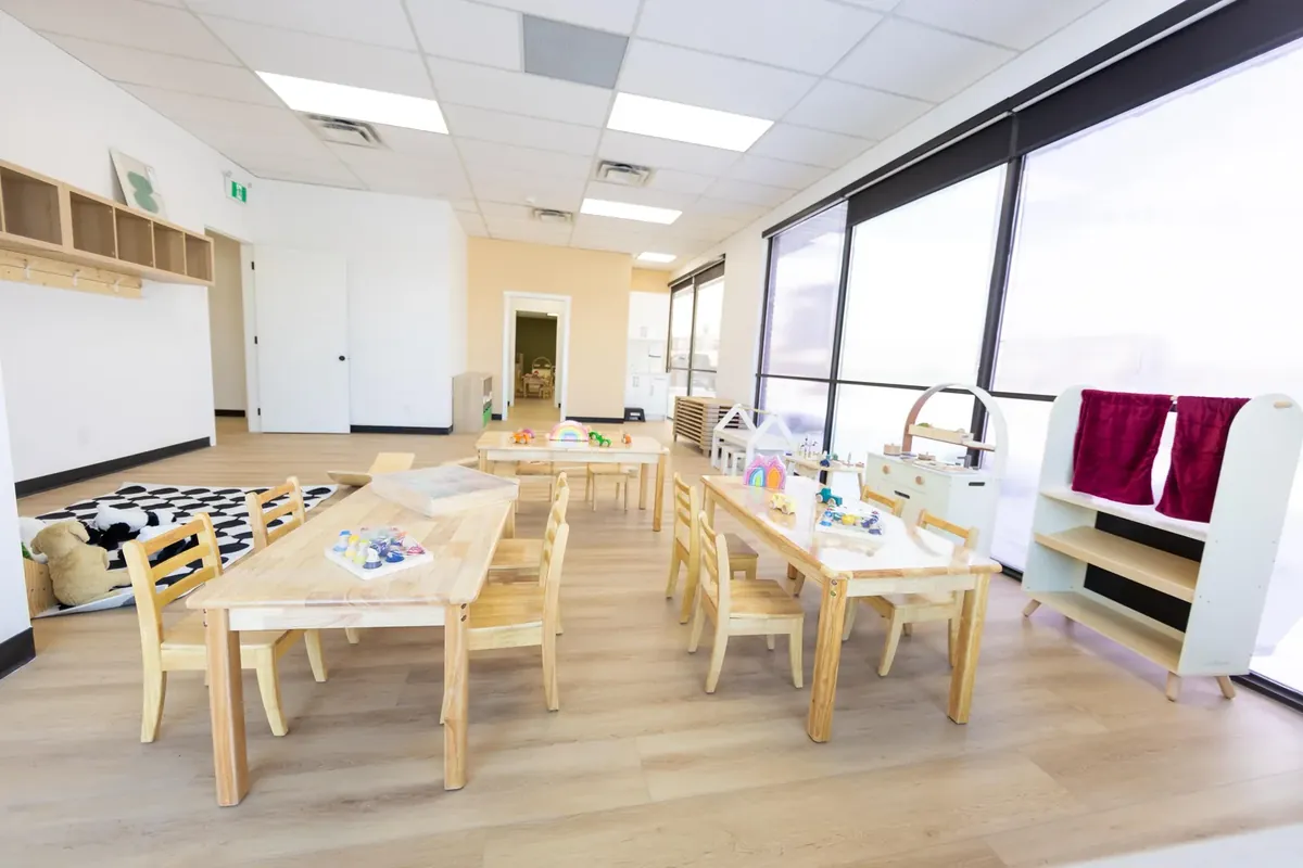 One of our classrooms: long low wooden tables and chairs, a play kitchen and a wall of large windows