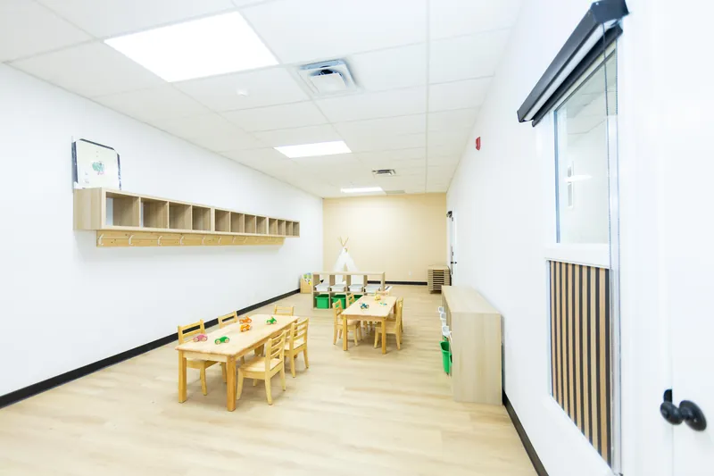 A bright classroom with cubbies, low tables and a tipi at the far end