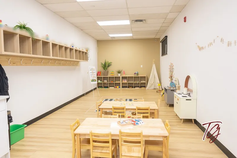 A long classroom with cubbies, low tables, a tipi and a play kitchen