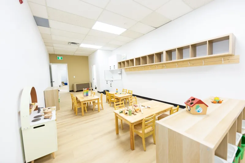 A classroom with shelves, a play kitchen, low tables and cubbies