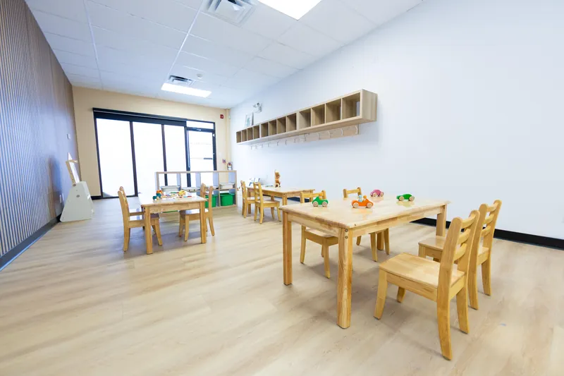 A classroom with low tables, toy cars and a wall of windows
