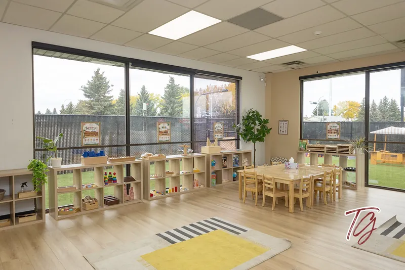 A classroom with shelves, a table and a yellow rug, with the playground outside the windows