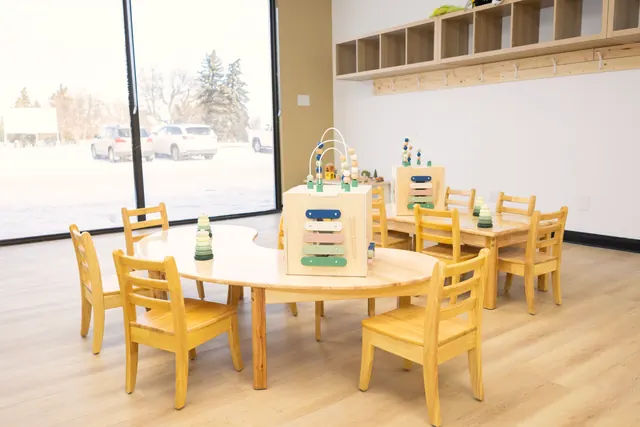Kidney-shaped child-size table with wooden chairs beside a large window