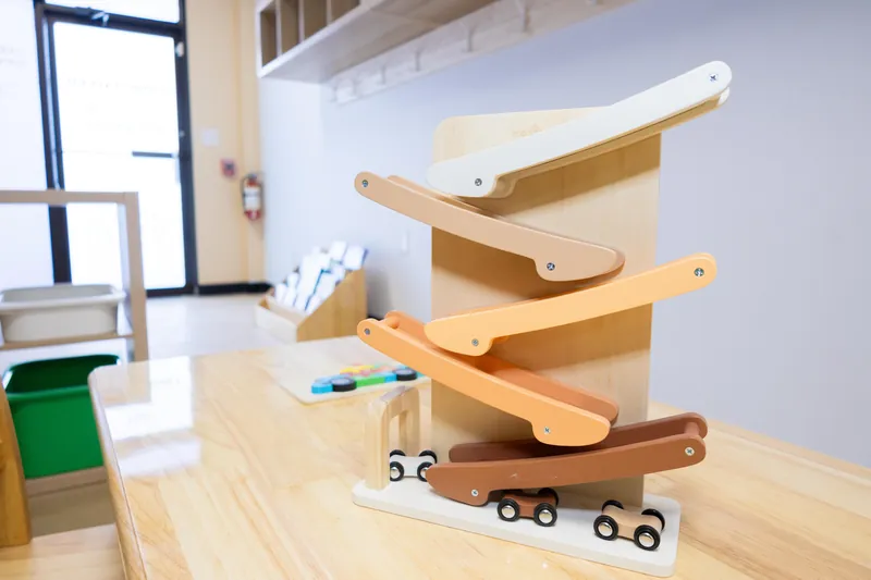 A wooden toy ramp with painted slides and small wooden cars on a low table in a classroom